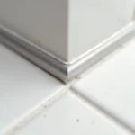 Cornière aluminium anodisé argenté posée sur le chant coupé d'un carrelage blanc dans une salle de bain moderne