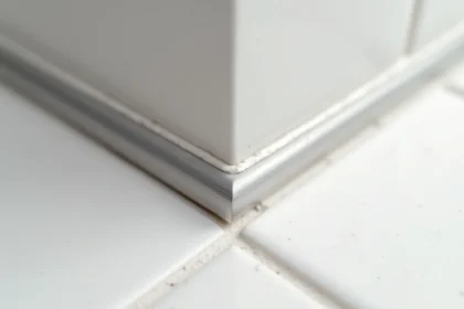 Cornière aluminium anodisé argenté posée sur le chant coupé d'un carrelage blanc dans une salle de bain moderne